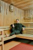 Der Schauspieler Guido Drell sitzt in einem schwarzen Anzug mit schwarzem Hemd auf einer hölzernen Bank in einer finnischen Sauna