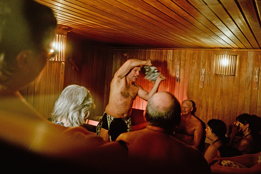 Das Foto entstand in einer Sauna. Im Publikum steht ein oberkörperfreier Schauspieler, der ein Handtuch durch die Luft schlägt.