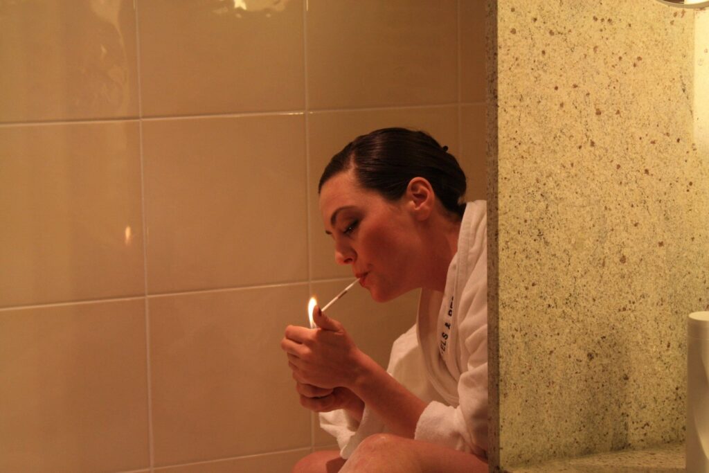Auf dem Bild ist eine Frau mit Bademantel im Bad, die sich eine Zigarette anzündet.