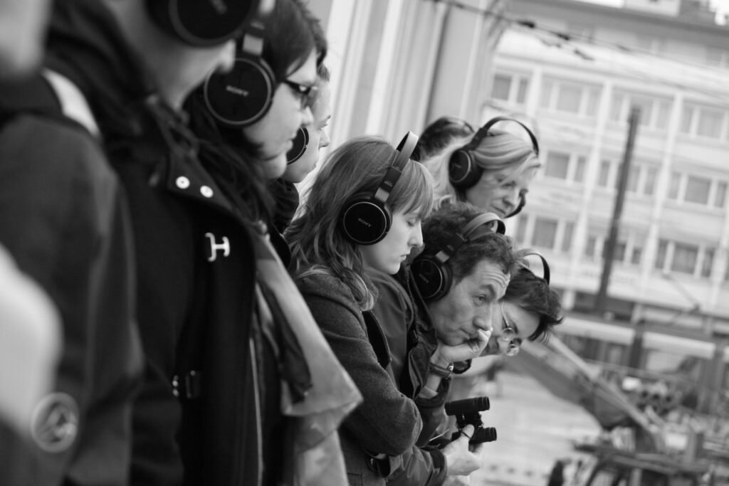 Auf dem schwarz-weißen Foto sind mehrere Menschen mit Kopfhörern zu sehen.