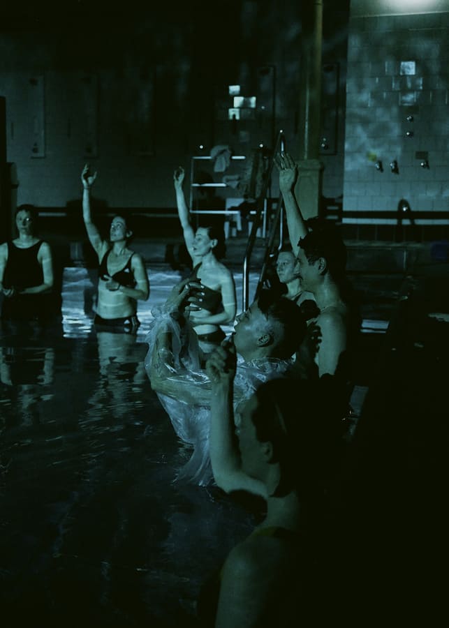 Auf dem dunklen Foto ist das Publikum im Wasser stehend zu sehen. Sie strecken alle den Arm nach oben.