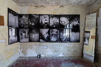 Auf dem Foto ist eine schwarzweiße Bilderserie an einer alten Wand zu sehen. Rechts davon steht ein Spiegel.