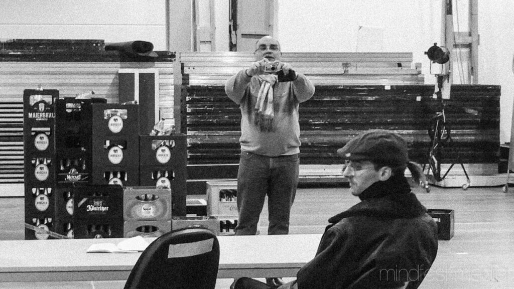 Auf dem schwarzweißen Foto ist ein Mann der ein Foto von einem vor ihm sitzenden Mann macht.