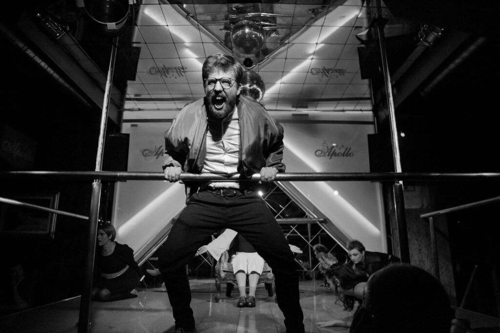 Auf dem schwarzweißen Foto hält sich ein Mann brüllend an einem Geländer auf einer Bühne fest.