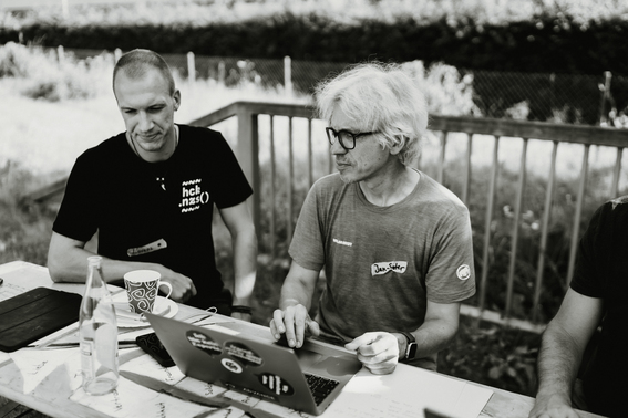 Auf dem schwarzweißen Foto sieht man zwei Männer draußen vor einem Computer sitzen.