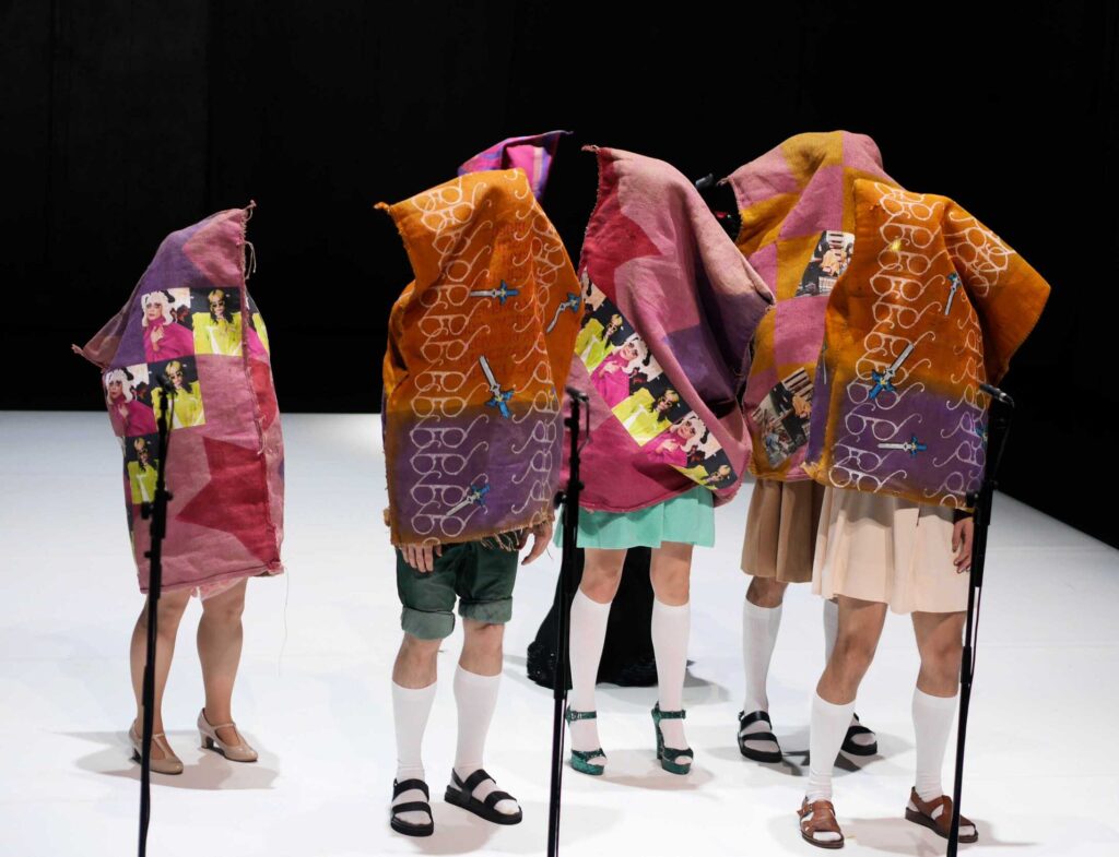 Auf dem Foto sind mehrere Menschen mit bunten Säcken über dem Kopf. Sie tragen weiße Kniestrümpfe in Sandalen.