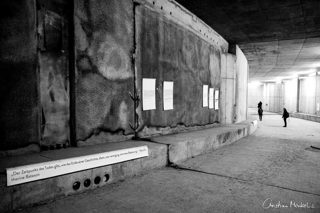 Auf dem Foto ist ein rundum betonierter, runder Gang. An den Wänden hängen Texte und Zitate.
