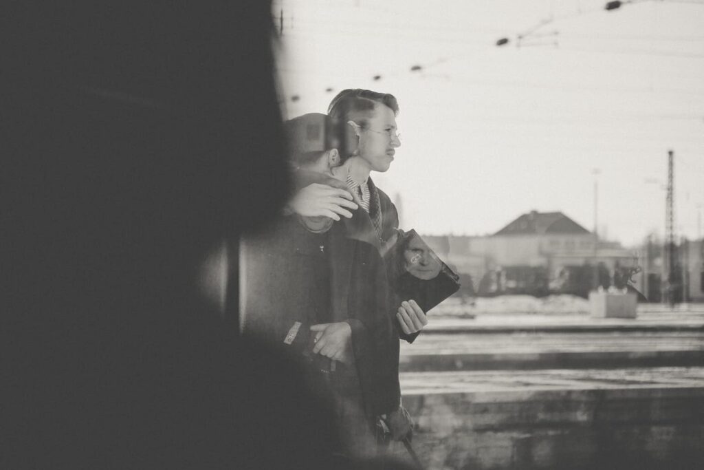 Auf dem schwarzweißen Foto sieht man durch eine Zugscheibe einen Mann mit einer Frau im Arm und einer Tasche in der Hand.