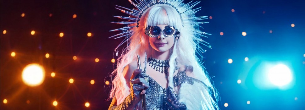 Auf dem Banner ist eine Frau mit silbernem Kleid und einer Strahlenkrone zu sehen. Hinter ihr sind orange und blaue Lichter.