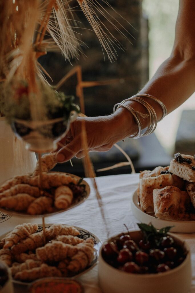 Das Bild zeigt einen Teil des liebevoll gestalteten Buffets des Selbstliebe-Festivals. Ein mit silbernen Armreifen geschmückter Arm nimmt greift von rechts in das Bild und nimmt sich eine Mini-Nussecke von einer Etagere.